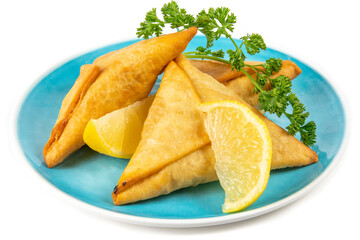 Three golden brown samosas on a blue plate with lemon and parsley garnish isolated on white