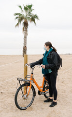 Fototapeta premium young girl wearing protective mask walks along the beach with her vintage orange bike