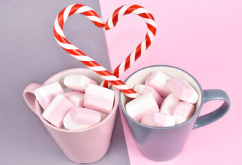 Happy Valentine day concept. Coffee mugs with marshmallow, heart made of lollipops. Gray and pink background. Festive card for 14 February.
