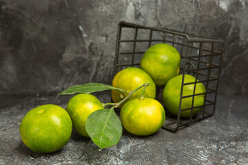 Horizontal view of fallen basket with fresh green tangerines on gray background