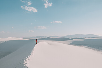 A girl in a long flowing red skirt walking the white gypsum sand dunes of White Sands National Park, New Mexico, USA 