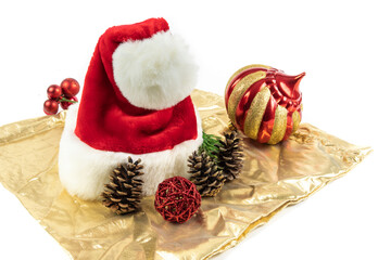 a red Santa Clause hat with Christmas decorations on a gold colored satin cloth