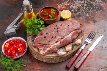 Above view of red meat on wooden tray and garlic green ketchup and chopped pepper oil bottle on dark background