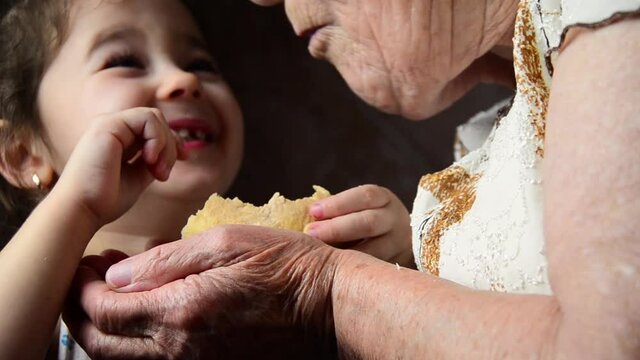 A small child feeds his grandmother with bread crumbs. The child feeds the old grandmother. The grandmother eats bread from the hands of a small child. Social advertising of poverty and hunger.