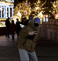  Young guy dressed in winter clothes on his head a hood and a face mask, shows gesture excellent. 