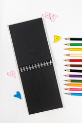 black notepad spiral colored pencils on white background