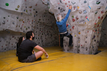 Climbing instructor wearing protective face mask showing how to climb a wall to his students....