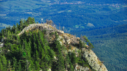 A rocky mountain peak rising spectacular above Olt Valley and surrounding forested hills. A Christian Cross was placed on the top of the crest. Cozia National Park, Carpathian Mountains, Romania. © Alexandru V