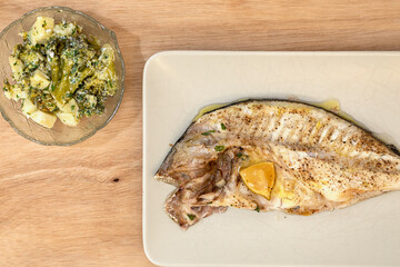 A rectangular plate with gilthead bream and a bowl with broccoli and potatoes.
