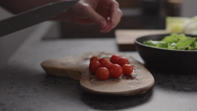 Slow motion man hand cutting cherry tomatoes into halves on wood board on home kitchen
