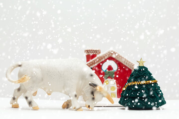 Toy bull, a symbol of the new year 2021, a toy house at the Christmas tree. Winter, it's snowing. Happy New Year. Greeting card ideas. Copy space. Mock up