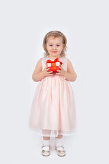 A beautiful little girl in a ball gown with a gift in her hands stands full-length on a white background.