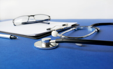 Medical stethoscope and clipboard with a blank sheet of paper on a blue background. View from above. Medical concept.