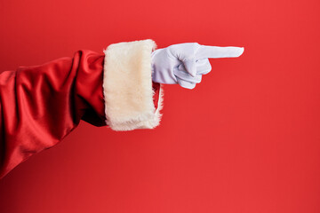 Hand of a man wearing santa claus costume and gloves over red background pointing with index finger to the side, suggesting and selecting a choice