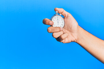Hand of young hispanic man using stopwatch over isolated blue background.