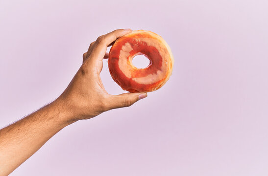 Hand of hispanic man holding donut over isolated pink background.
