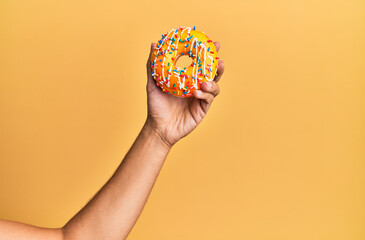Fototapeta na wymiar Hand of hispanic man holding donut over isolated yellow background.
