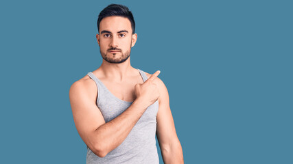 Young handsome man wearing swimwear and sleeveless t-shirt pointing with hand finger to the side showing advertisement, serious and calm face