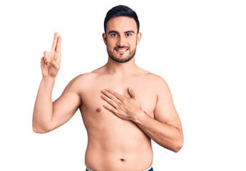 Young handsome man wearing swimwear smiling swearing with hand on chest and fingers up, making a loyalty promise oath