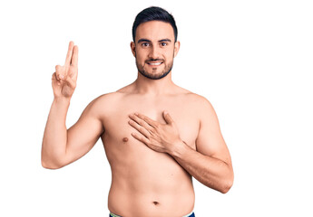 Young handsome man wearing swimwear smiling swearing with hand on chest and fingers up, making a...