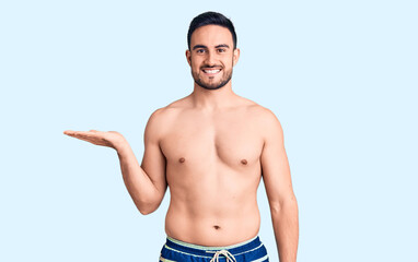 Young handsome man wearing swimwear smiling cheerful presenting and pointing with palm of hand looking at the camera.