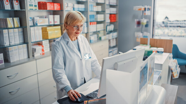 Pharmacy Drugstore Checkout Counter Cashier: Portrait of Experienced Caucasian Female Pharmacist Using Personal Computer, to Check Stock Inventory of Medicine, Drugs, Vitamins, Health Care Product