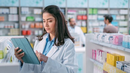 Pharmacy Drugstore: Beautiful Latina Pharmacist Uses Digital Tablet Computer, Checks Inventory of...