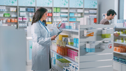 Pharmacy Drugstore: Beautiful Latina Pharmacist Uses Digital Tablet Computer, Checks Inventory of Medicine, Drugs, Vitamins, Health Care Products on a Shelf. Professional Pharmacist in Pharma Store
