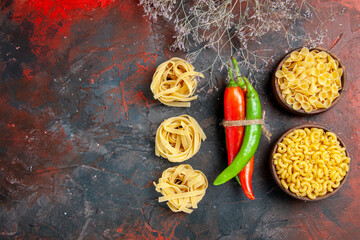 Top view of uncooked pastas cayenne peppers in different colors and sizes tied in one another with rope on mixed color table