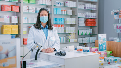 Pharmacy Drugstore Checkout Cashier Counter: Portrait of Beautiful Young Latin Female Pharmacist Wearing Protective Face Mask Looks at the Camera. Store with Medicine, Drugs, Vitamins.