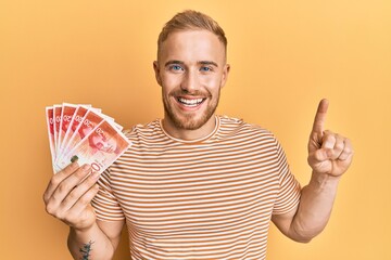 Young caucasian man holding 20 israel shekels banknotes smiling with an idea or question pointing...