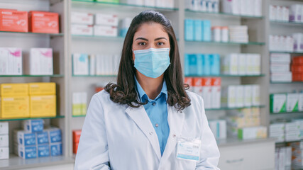Fototapeta na wymiar Pharmacy Drugstore Checkout Cashier Counter: Portrait of Beautiful Young Latin Female Pharmacist in Protective Face Mask Looks at the Camera, Smiles Charmingly. Store with Medicine, Drugs, Vitamins.