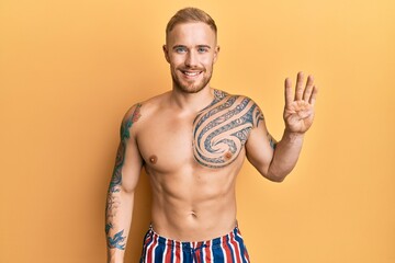 Young caucasian man wearing swimwear shirtless showing and pointing up with fingers number four while smiling confident and happy.
