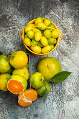 Vertical view of a basket and bucket full of fresh green tangerines cut in half and peeled tangerine on gray background stock photo