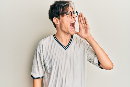 Young hispanic man wearing casual clothes and glasses shouting and screaming loud to side with hand on mouth. communication concept.