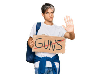 Young hispanic man holding no guns warning banner with open hand doing stop sign with serious and...