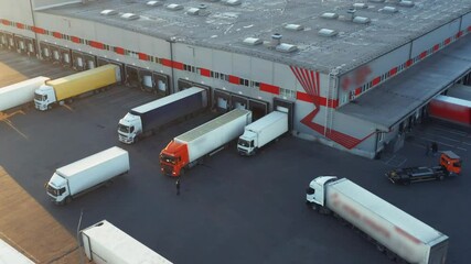 Trucks with semi-trailers stand at warehouse ramps in the logistics park with loading hub and wait for load and unload goods at sunset. Aerial view - Powered by Adobe