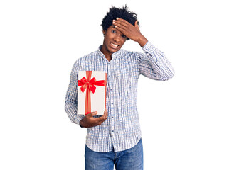 Handsome african american man with afro hair holding gift stressed and frustrated with hand on head, surprised and angry face