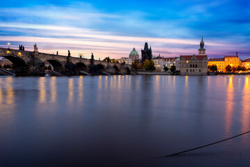 Fototapeta premium Charles Bridge on the Vltava River at sunset and colorful clouds and lights on the bridge in the early evening in the center of Prague