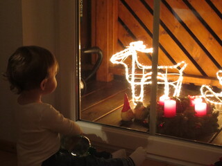 Little boy watching the lights of Christmas decoration through the balcony window.