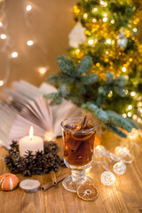 Mulled wine with cinnamon sticks and orange on a wooden table. Burning candle and Christmas tree lights