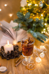 Mulled wine with cinnamon sticks and orange on a wooden table. Burning candle and Christmas tree lights