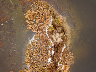 Aerial drone top view. The grassy island is lightly covered with snow. Thin ice on the water.