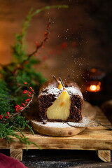 Chocolate pear sponge cake with whole fruits, wooden rustic table. Pear pie with christmas tree brush, candle. Winter homemade dessert. Copy space, selective focus.