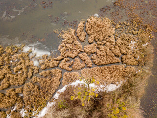 Aerial drone top view. The grassy island is lightly covered with snow. Thin ice on the water.