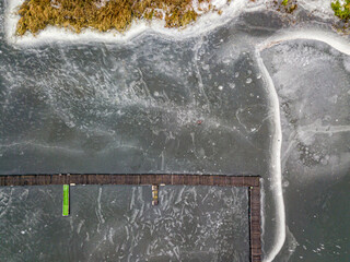 Aerial drone top view. Fisherman on the ice near the pier. Frosty pattern on thin ice. Wooden pier in ice.