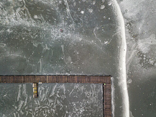 Aerial drone top view. Fisherman on the ice near the pier. Frosty pattern on thin ice. Wooden pier in ice.