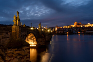 Fototapeta premium old illuminated prague castle and charles bridge and st. vita church lights from street lights are reflected on the surface of the vltava river in the center of prague at night in the czech republic