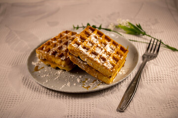 Homemade waffles with powdered sugar. Viennese waffles with a fork. Close-up. Delicious dessert or breakfast.