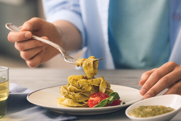 Woman eating pasta with pesto sauce in kitchen